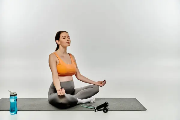 A pregnant woman in activewear sits on a yoga mat, taking a break to drink water. — Stock Photo