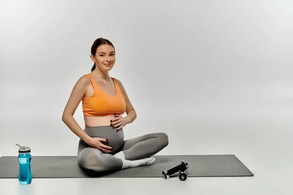 Una donna incinta in stato di usura attiva siede su un tappetino yoga vicino a una bottiglia d'acqua. — Foto stock