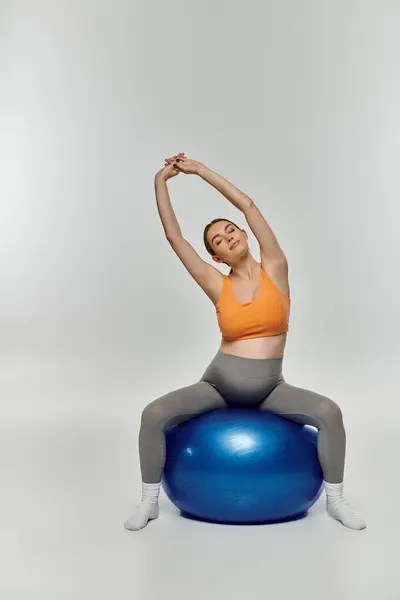 Sporty pregnant woman in active wear balancing on top of a bright blue exercise ball. — Stock Photo