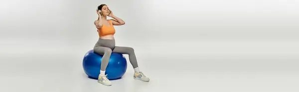Eine schwangere Frau in Aktivkleidung sitzt anmutig auf einem blauen Turnball und zeigt Kraft und Gleichgewicht. — Stockfoto