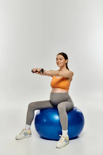 Eine schwangere Frau in Aktivkleidung sitzt auf einem Übungsball und balanciert konzentriert. — Stockfoto