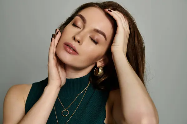 A woman in a green top holds her head, lost in thought against a simple backdrop. — Stock Photo