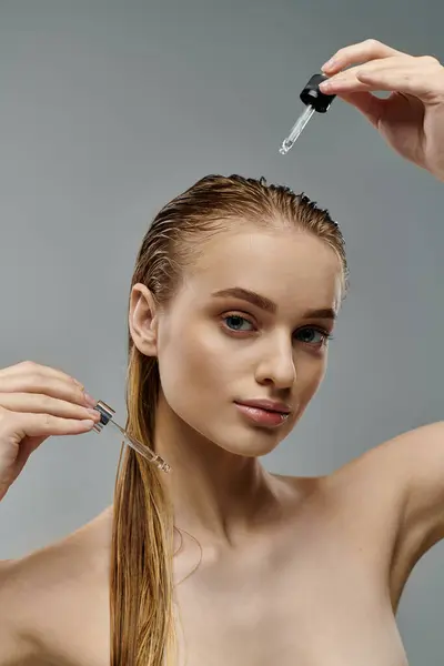 Young woman using hair oil on gray backdrop. — Foto stock