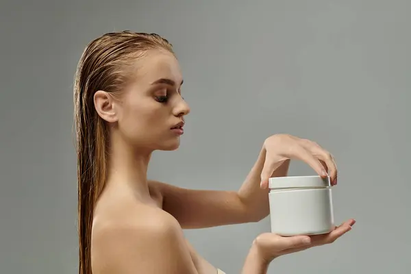 Uma jovem mulher bonita mostrando sua rotina de cuidados com o cabelo com o cabelo molhado, segurando um recipiente. — Fotografia de Stock