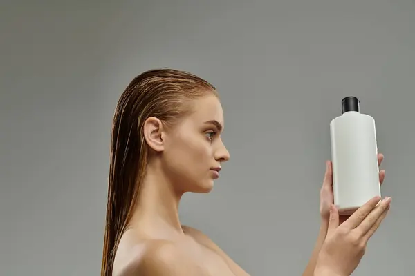 A young woman with wet hair delicately holds a bottle of shampoo in her hand. — Stock Photo