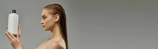Uma jovem mulher segura uma garrafa de produto de cuidados com o cabelo, mostrando sua rotina de beleza com o cabelo molhado. — Fotografia de Stock