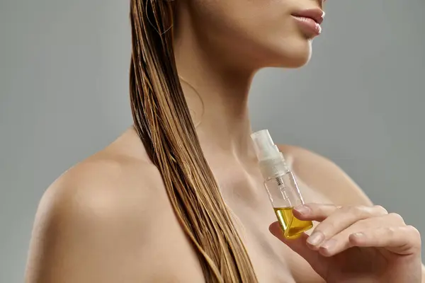 Молодая женщина, держащая бутылку масла, демонстрирует свой уход за волосами с мокрыми волосами. — стоковое фото