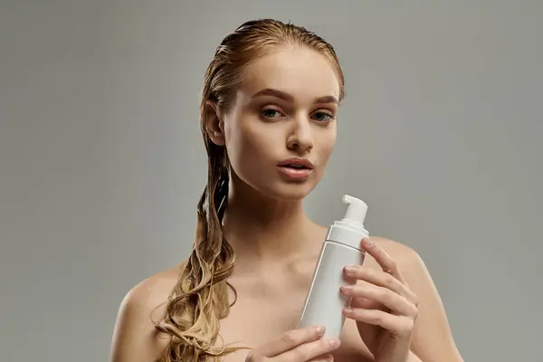 A young woman with wet hair holds a bottle of lotion in her hands, showcasing her hair care routine. — Stock Photo