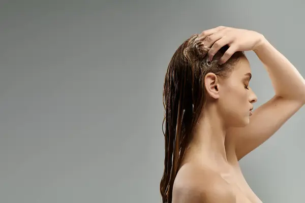 Langhaarige Schönheit enthüllt ihre Haarpflege-Routine vor grauem Hintergrund. — Stockfoto