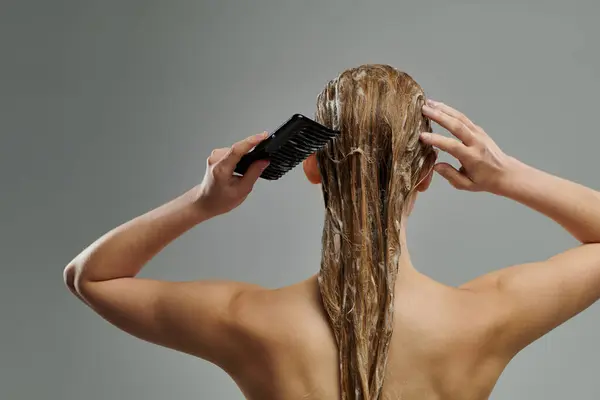 Uma jovem segura uma escova de cabelo, penteando o cabelo molhado com cuidado. — Fotografia de Stock