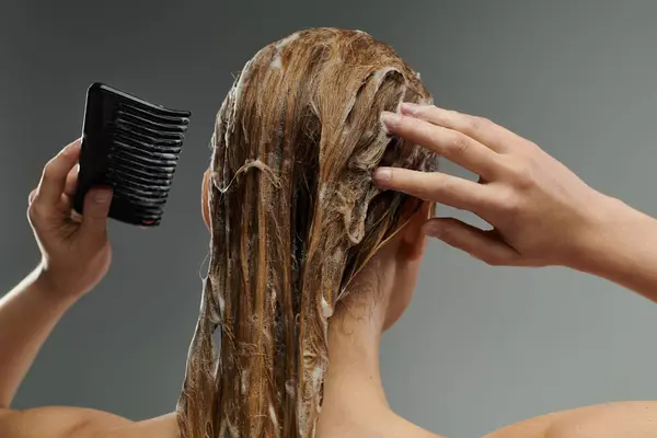 Una giovane donna si sta spazzolando i capelli con un pettine dopo un lavaggio dei capelli. — Foto stock