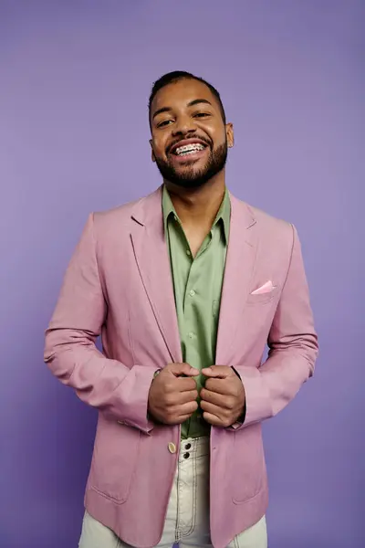 Стильний молодий чоловік з брекетами посміхається, одягнений у рожевий піджак і зелену сорочку на яскраво-фіолетовому тлі. — стокове фото