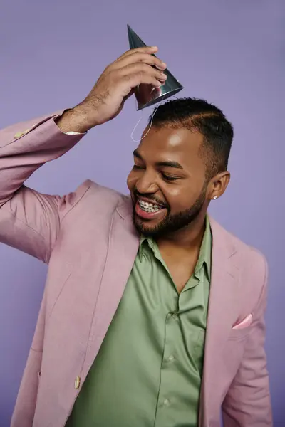 Ein fröhlicher, junger afroamerikanischer Mann posiert selbstbewusst in rosa Anzug und grünem Hemd vor lila Hintergrund. — Stockfoto