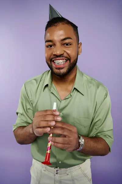 Young African American man in braces joyfully holds toothbrush while wearing party hat on purple background. — Stock Photo