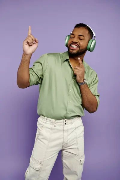 Un jeune Afro-Américain avec des bretelles pointe joyeusement sur le côté tout en portant un casque sur un fond violet. — Photo de stock