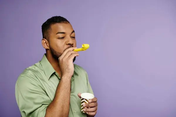Un giovane afroamericano in camicia verde che soffia corno su uno sfondo viola. — Foto stock