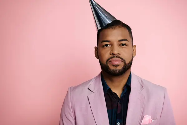 Joven hombre afroamericano lleva un sombrero de fiesta sobre un fondo rosa vibrante. - foto de stock