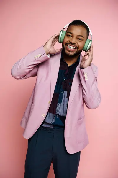 A happy, young African American man wearing braces listens to headphones in a pink jacket on a pink background. — Stock Photo