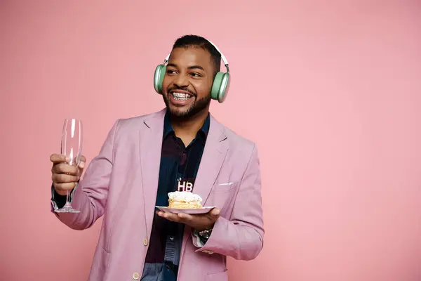 Young African American man in braces joyfully holds birthday cake while listening to music on headphones. — Stock Photo