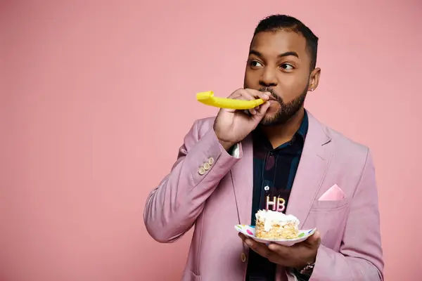 A stylish young African American man in a pink suit happily savors a piece of cake on a vibrant pink background. — Stock Photo