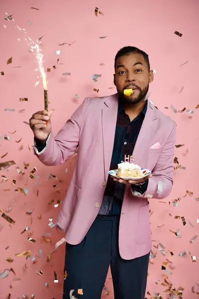 Junger Afroamerikaner in pinkfarbener Jacke hält in einem feierlichen Moment freudig eine Torte und Wunderkerze in der Hand. — Stockfoto