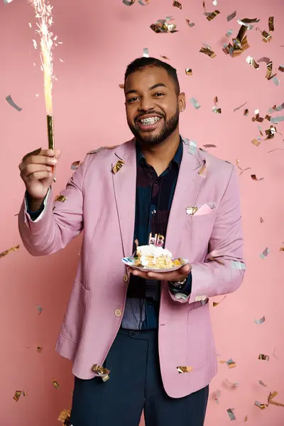 Junger afroamerikanischer Mann in pinkfarbener Jacke hält eine Wunderkerze auf einem leuchtend rosa Hintergrund und drückt damit sein Glück aus. — Stockfoto