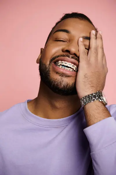 A young African American man smiling brightly, showcasing his braces, against a vibrant pink background. — Stock Photo