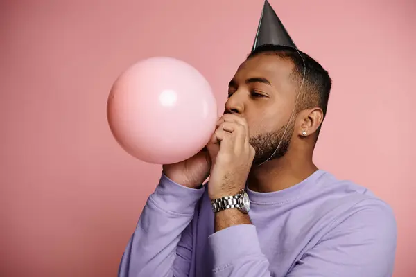 Junger Afroamerikaner mit Zahnspange lässt fröhlich einen Luftballon aufsteigen, während er einen bunten Partyhut trägt. — Stockfoto