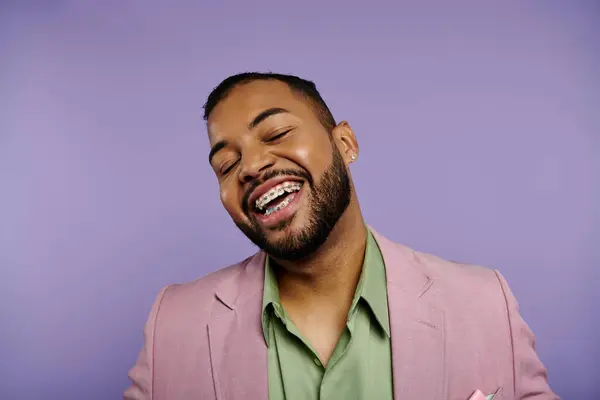 Молодий афроамериканський чоловік у костюмі радісно сміється з закритими очима на яскравому фіолетовому тлі. — стокове фото