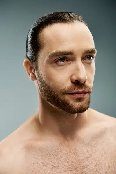 A shirtless man exuding masculinity and confidence, showcasing his rugged beard in a studio setting against a grey background. — Stock Photo