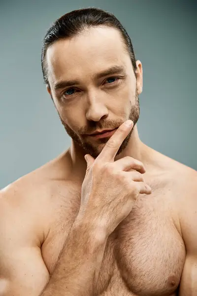 A handsome shirtless man with a beard striking a confident pose against a grey studio backdrop. — Stock Photo
