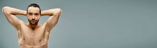 A shirtless man with a beard reclines with his hands behind his head in a serene pose on a grey background in a studio. — Stock Photo