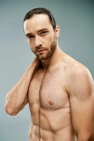 A fierce, shirtless man with a beard striking a confident and bold pose against a grey studio backdrop. — Stock Photo