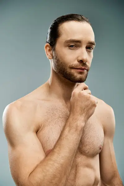 A shirtless man with a beard strikes a confident pose in a studio against a grey background. — Stock Photo