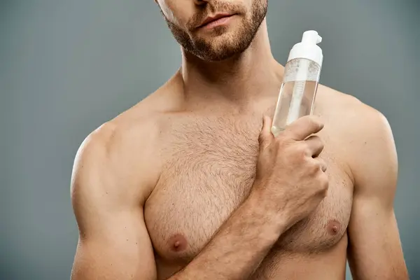 Ein gutaussehender Mann ohne Hemd und Bart hält eine Flasche Gesichtsreiniger in der Hand — Stockfoto