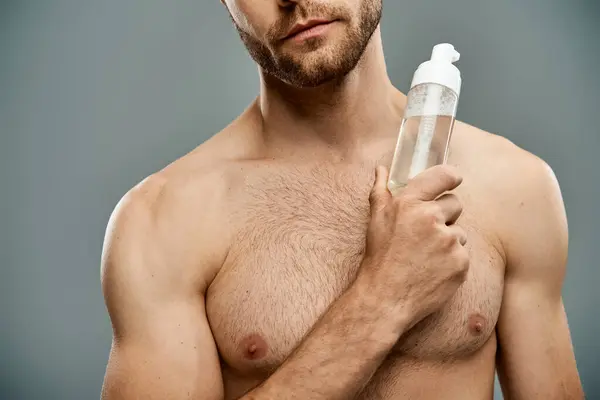 A handsome, shirtless man with a beard holds a bottle of facial cleanser — Stock Photo