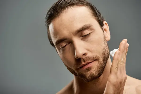 Shirtless man applying foam on face with beard in a stylish studio setting. — Stock Photo