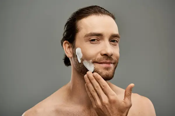 Ein Mann ohne Hemd und Bart mit Schaumstoff im Gesicht in einem Studio vor grauem Hintergrund. — Stockfoto