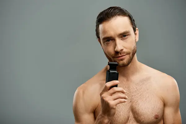Shirtless man with beard holding a perfume bottle against a grey studio backdrop. — Stock Photo