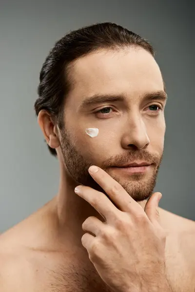 Un bel homme torse nu avec une barbe applique un masque crème sur son visage dans un décor de studio. — Photo de stock