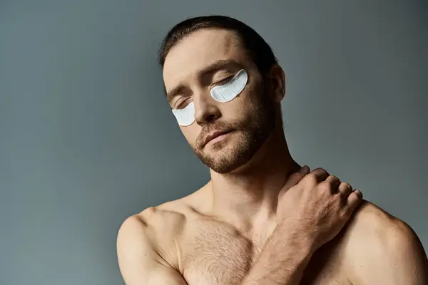 A shirtless, bearded man adorned with eye patches exudes a captivating yet mysterious aura against a neutral studio backdrop. — Stock Photo