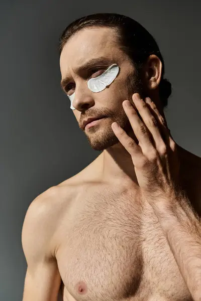 Handsome, shirtless man with patches on his face stands in a captivating pose on a grey studio background. — Stock Photo
