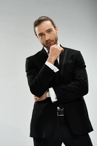 A bearded businessman in a stylish suit and tie strikes a confident pose against a grey studio background. — Stock Photo