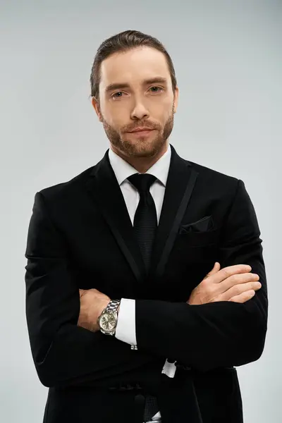 Um empresário barbudo em um terno elegante e gravata cruza confiantemente os braços contra um fundo de estúdio cinza. — Fotografia de Stock