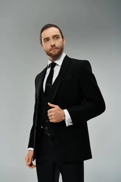A handsome, bearded businessman in a suit and tie strikes a confident pose in a studio against a grey background. — Stock Photo
