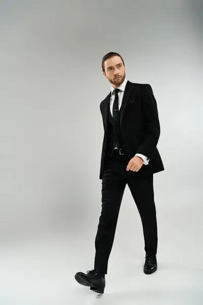 A bearded businessman confidently walks in a suit and tie against a grey studio backdrop. — Stock Photo