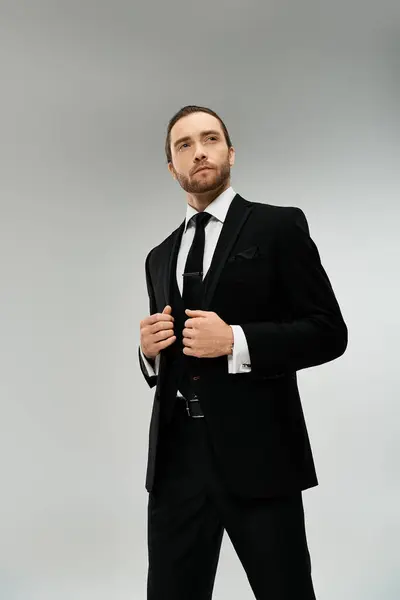 A stylish, bearded businessman in a suit and tie strikes a confident pose against a grey studio backdrop. — Stock Photo