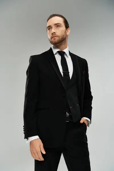 Handsome, bearded businessman in a suit and tie striking a confident pose against a grey studio background. — Stock Photo
