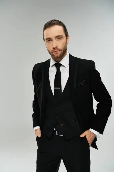 A handsome, bearded businessman in a suit and tie strikes a confident pose against a grey studio backdrop. — Stock Photo