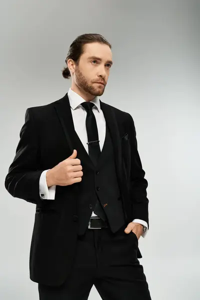 Бородатый, красивый бизнесмен в костюме и галстуке занимает уверенную позу на фоне серой студии. — стоковое фото